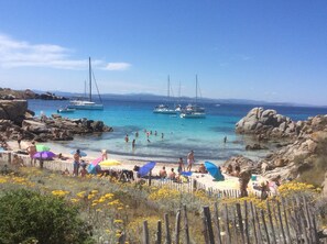 Uma praia com águas turquesa cristalinas, barcos e pessoas aproveitando a costa.