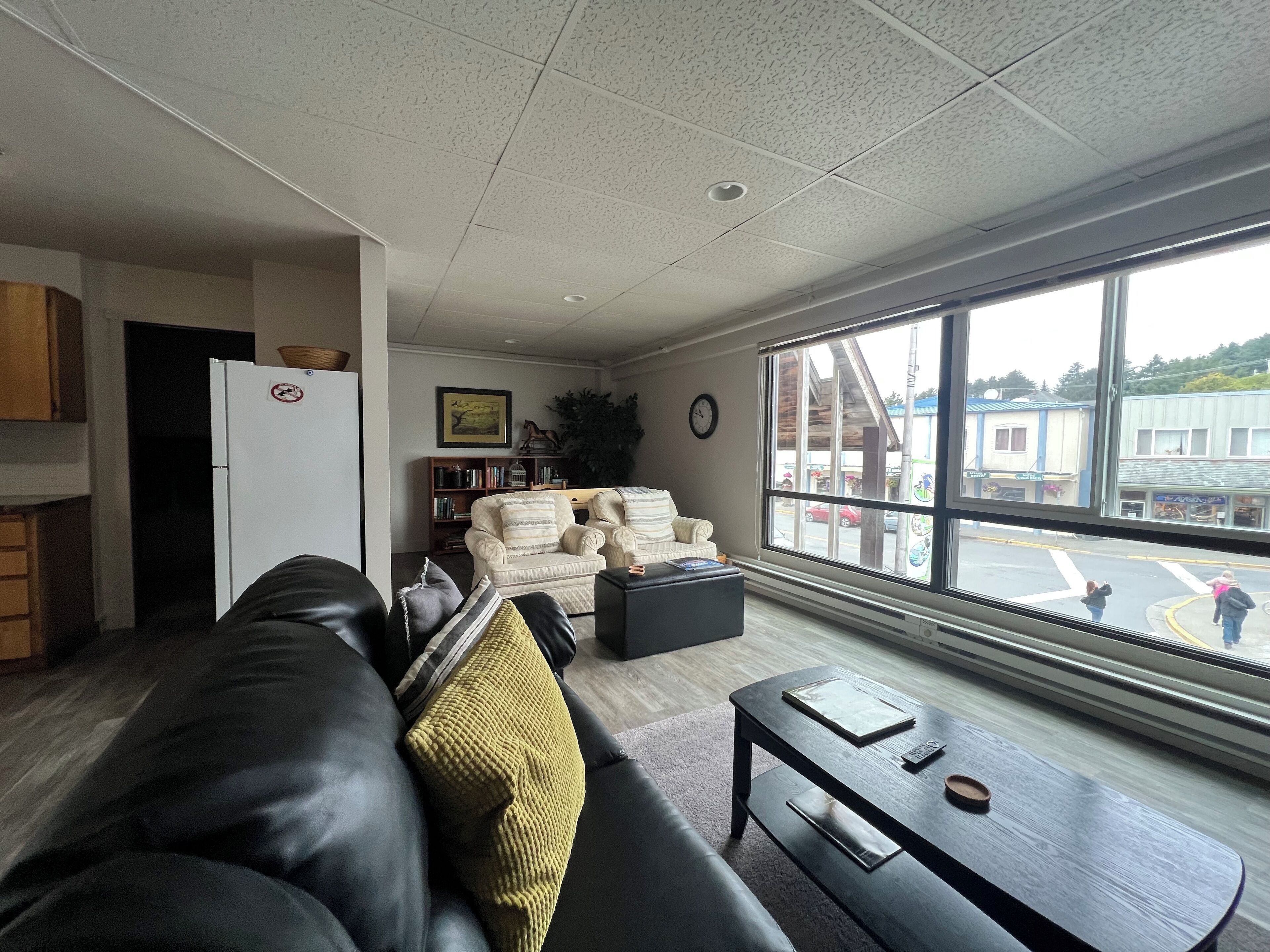 A living room with a leather sofa, a coffee table, and a large window offering a view of the street.