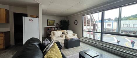A living room with a leather sofa, a coffee table, and a large window offering a view of the street.