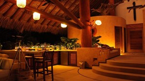 A bar area with a thatched roof, wooden furniture, and a cross on the wall.