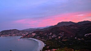 A coastal town with a beach, mountains in the background, and a sunset sky.