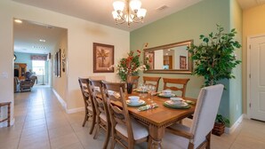 Uma sala de jantar com uma mesa de madeira posta para quatro pessoas, rodeada por cadeiras, um lustre e um espelho grande.