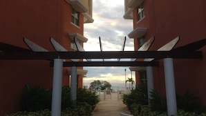 Un couloir agrémenté d’une pergola, qui mène à une entrée fermée par un portail.
