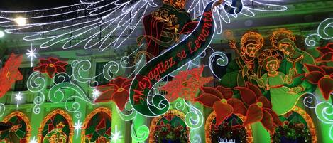 A festive outdoor display with illuminated figures and decorations, including a prominent winged figure and a banner reading "Magiiez se Levi."