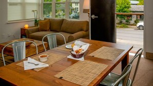 Uma zona de refeições moderna com uma mesa de madeira, cadeiras de metal e vista para a rua através de grandes janelas.