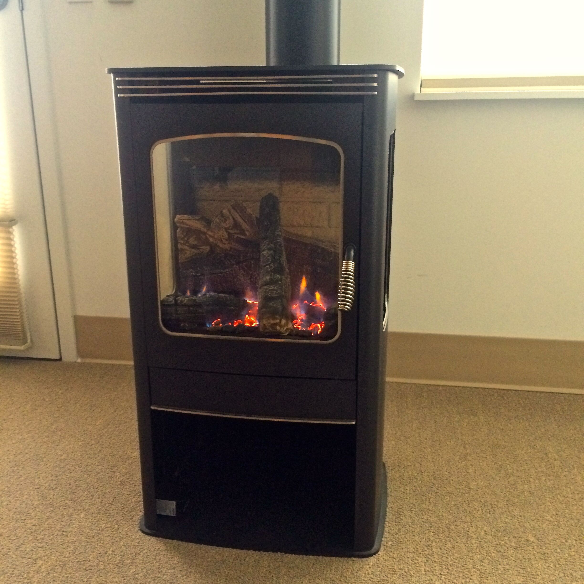 A black wood-burning stove with a glass door, visible flames, and a metal vent.
