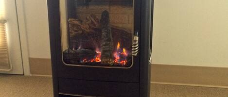 A black wood-burning stove with a glass door, visible flames, and a metal vent.