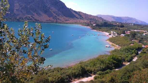 Un paysage côtier avec une mer bleue et limpide, des bateaux et une route menant à un village.