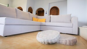 Un salon moderne avec un canapé d’angle aux couleurs claires, un pouf rond et une porte en bois en arrière-plan.
