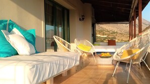 Une chambre à coucher avec un lit, deux fauteuils en osier blancs, une petite table avec des fruits, et une vue sur un paysage montagneux.