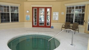 Una piscina interior con suelo de cristal, rodeada por paredes color beige y grandes ventanales.