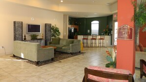 Un salón amplio con un sofá, sillas y un televisor. Se ve una cocina al fondo con una zona de comedor.