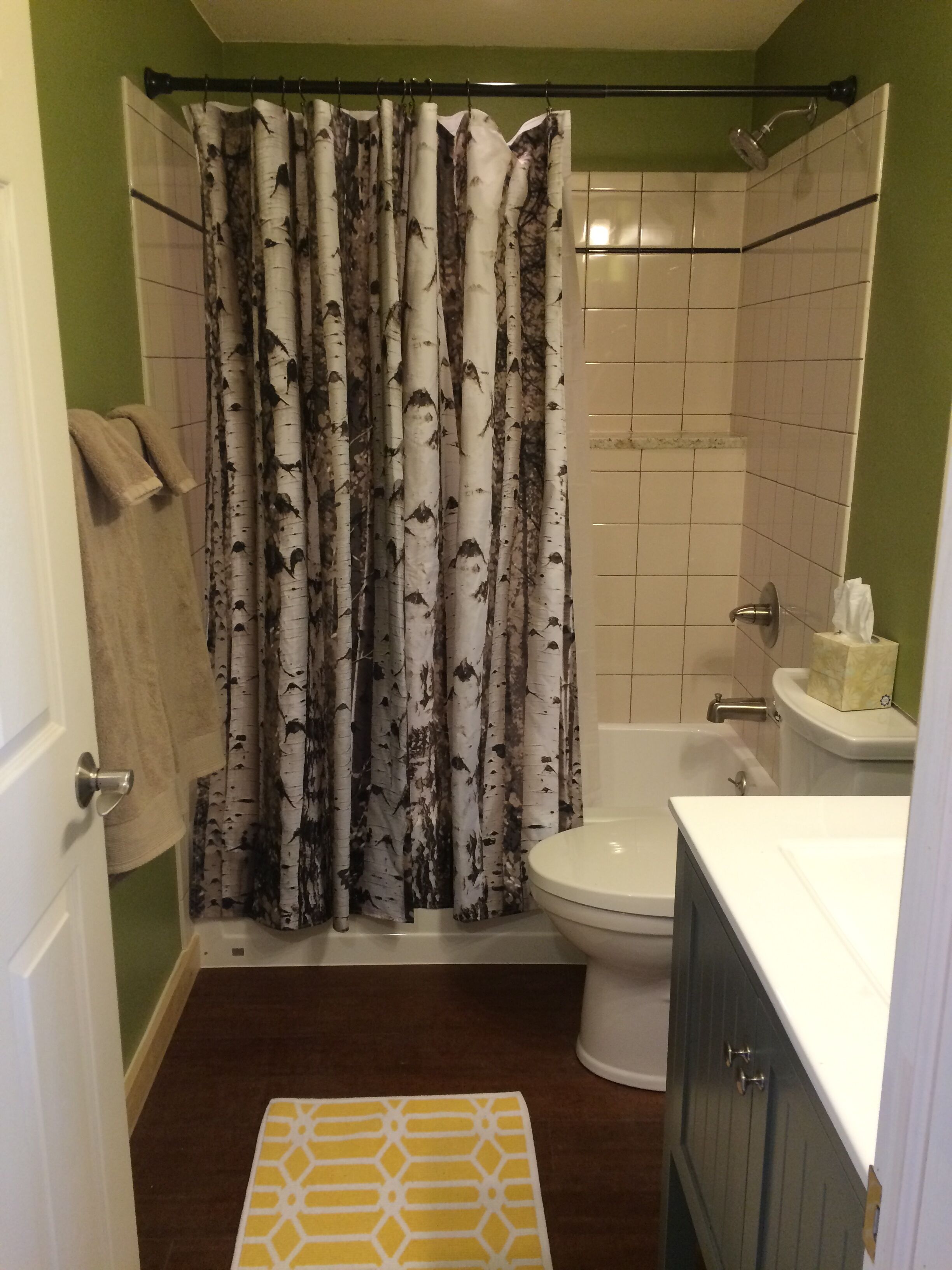 A bathroom with a birch-patterned shower curtain, a toilet, a sink, and a towel rack.