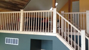 A wooden ceiling with a ceiling fan, a balcony with a railing, and a staircase leading to an upper level.