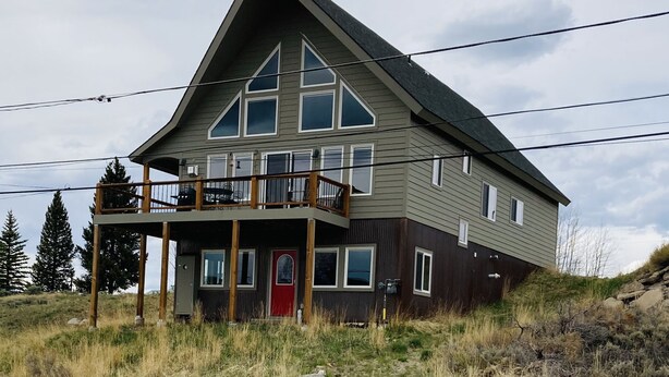 A large, two-story house with a balcony, a red door, and a wooden deck.
