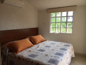 Ein Schlafzimmer mit einem Bett, zwei Kissen, einem Fenster und einer Klimaanlage.