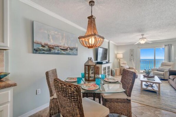 A dining area with wicker chairs, a glass table, and a hanging light fixture.