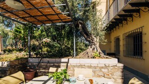 An outdoor dining area with a table set for breakfast, surrounded by stone walls and a large tree. - Charming Villa by the sea, wifi and cooking class free! (Termini Imerese)