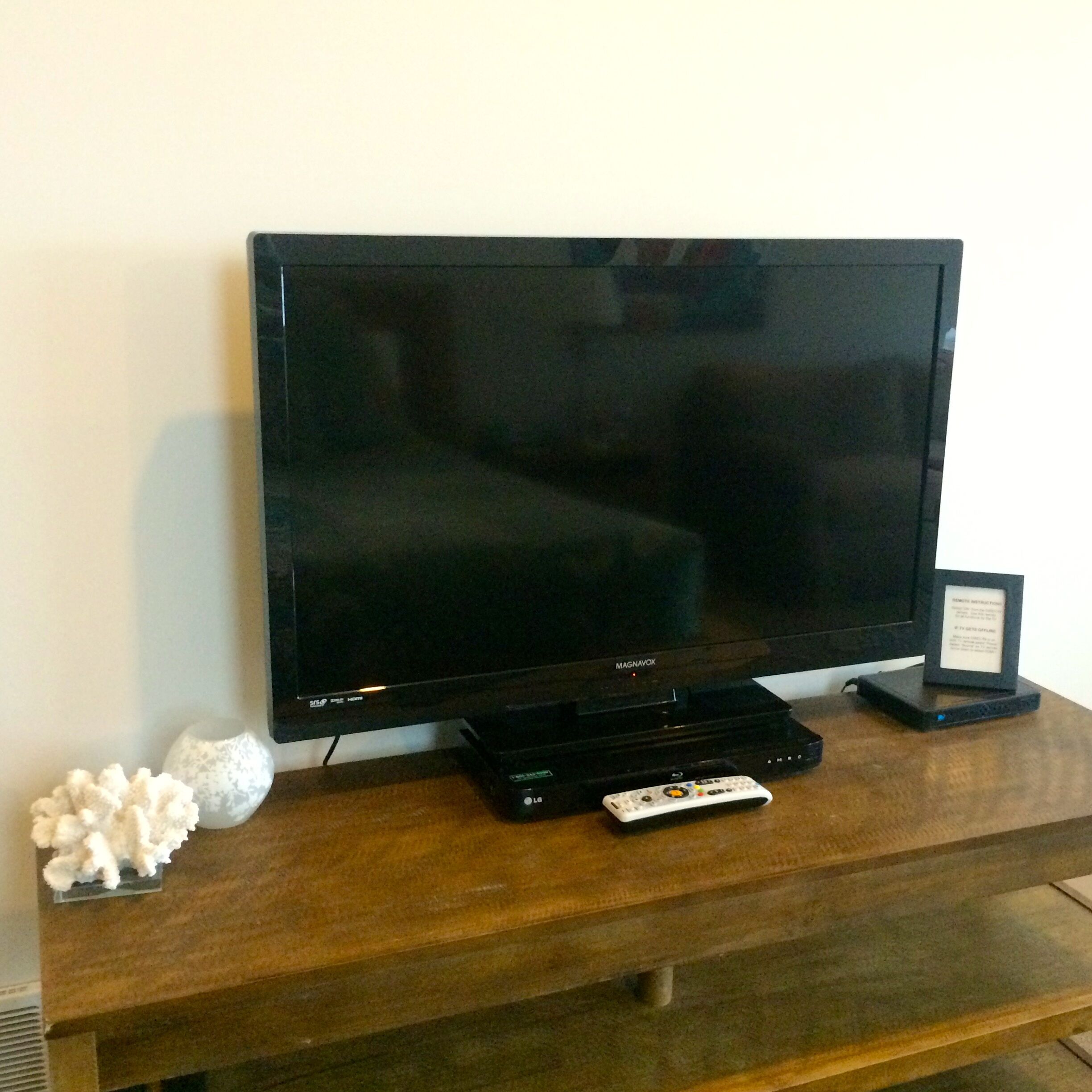 Un televisor de pantalla plana sobre un mueble de madera con un control remoto y un objeto pequeño enmarcado a la derecha.