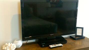 Un televisor de pantalla plana sobre un mueble de madera con un control remoto y un objeto pequeño enmarcado a la derecha.