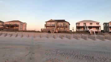 A beachfront property with multiple-story buildings, a sandy beach in the foreground, and a clear sky.