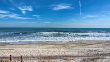 A beach with a wooden fence in the foreground and waves crashing onto the shore.