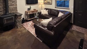 A living room with a stone fireplace, a leather sofa, a flat-screen TV, and a large window. - Private level of the home is located on a private 160 acre ranch  (Escalante)