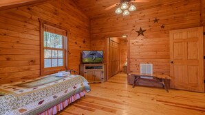 Ein Zimmer in einer Holzhütte mit einem Bett, einem Fernseher, einem Schreibtisch und einer Sternen-Dekoration an der Wand.