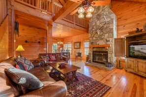 L’intérieur d’un chalet confortable, avec une cheminée en pierre, un canapé en cuir et un téléviseur.