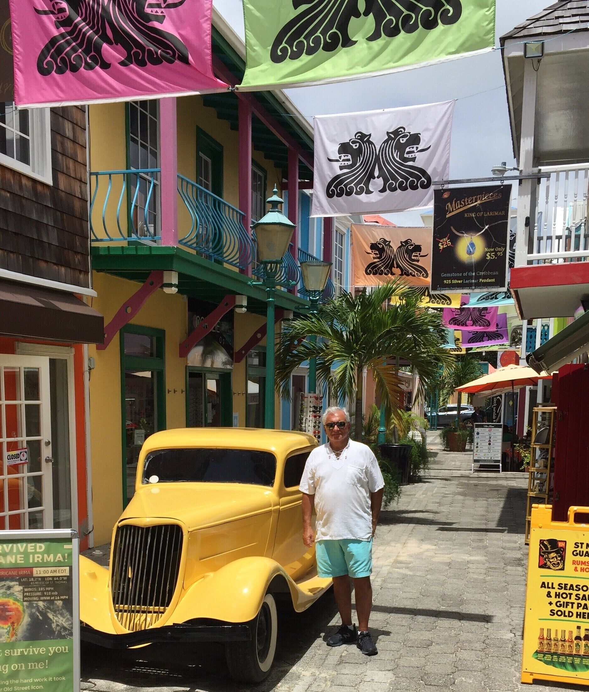 Un coche amarillo antiguo estacionado en una calle con edificios y pancartas coloridas.