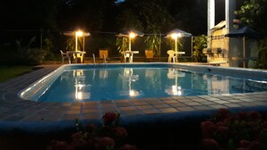 A swimming pool with tiled edges, surrounded by a brick patio. There are outdoor tables and chairs under umbrellas, and a fence enclosing the area. - Guicci Resort - Playa Corona beach  (San Carlos)