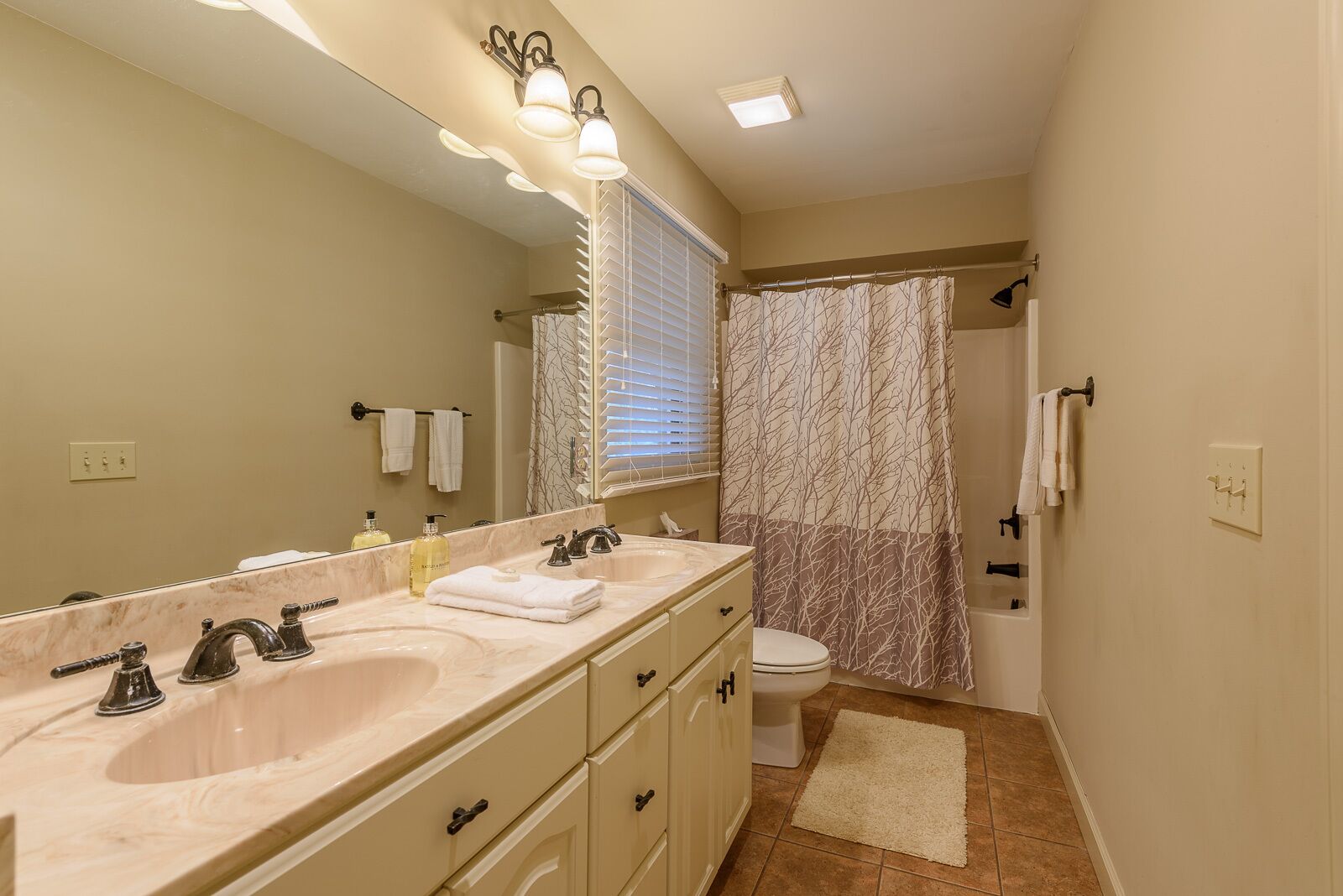 A bathroom with a double sink vanity, a toilet, a shower with a curtain, and a window with blinds.