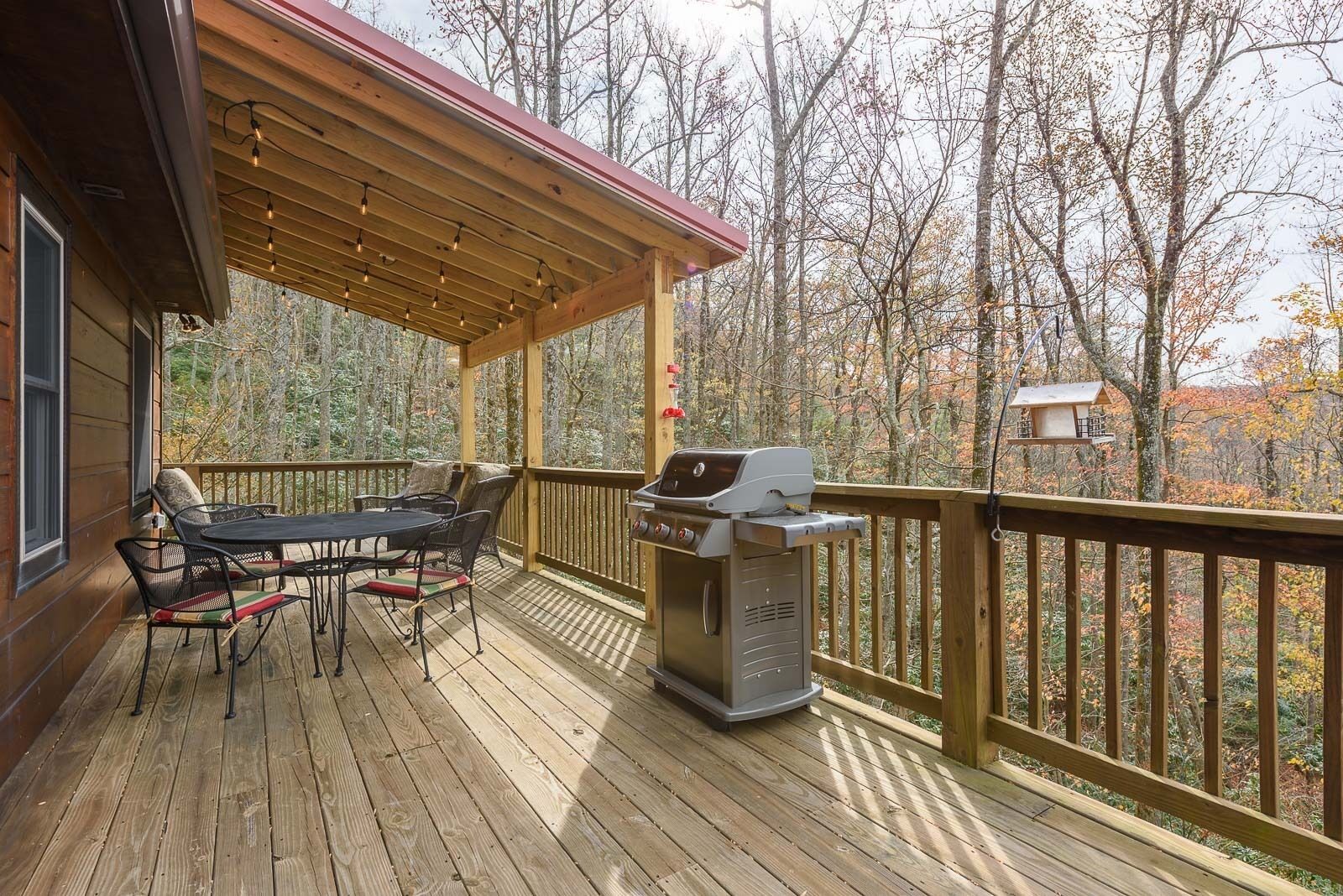 A wooden deck with a covered patio area, outdoor furniture, and a grill.