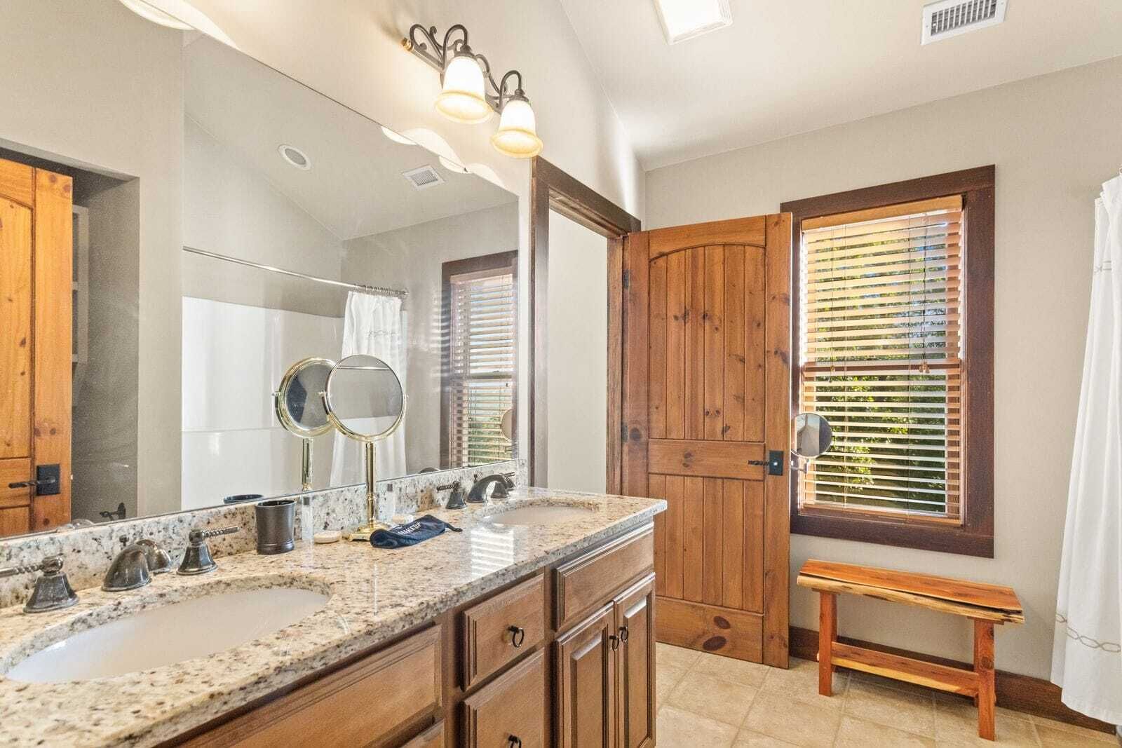 A bathroom with a granite countertop, two sinks, a large mirror, and wooden doors.