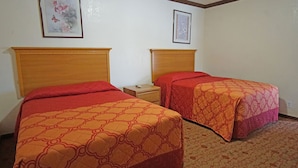 Deux lits simples avec des têtes de lit en bois, dans une chambre dont le sol est recouvert d’une moquette.