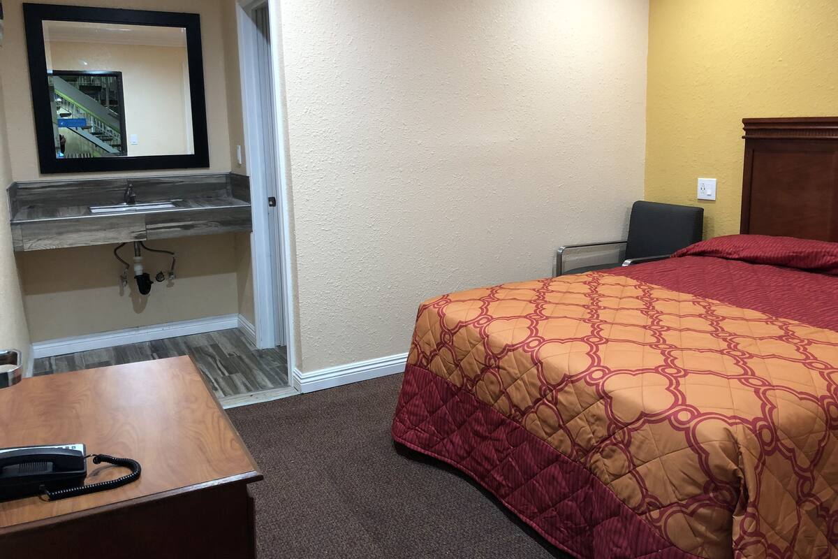 A hotel room with a bed, a desk with a telephone, a mirror, a sink, and a chair.