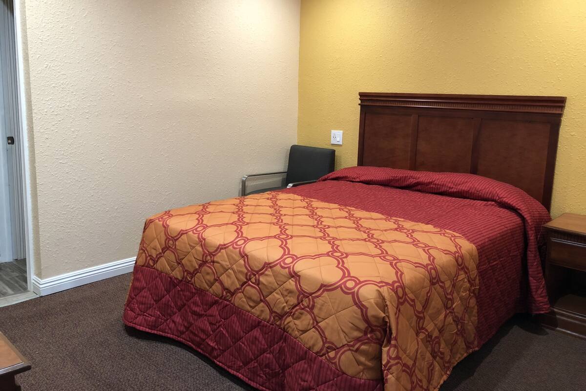 A single bed with a red and beige quilt, a wooden headboard, and a small bedside table.
