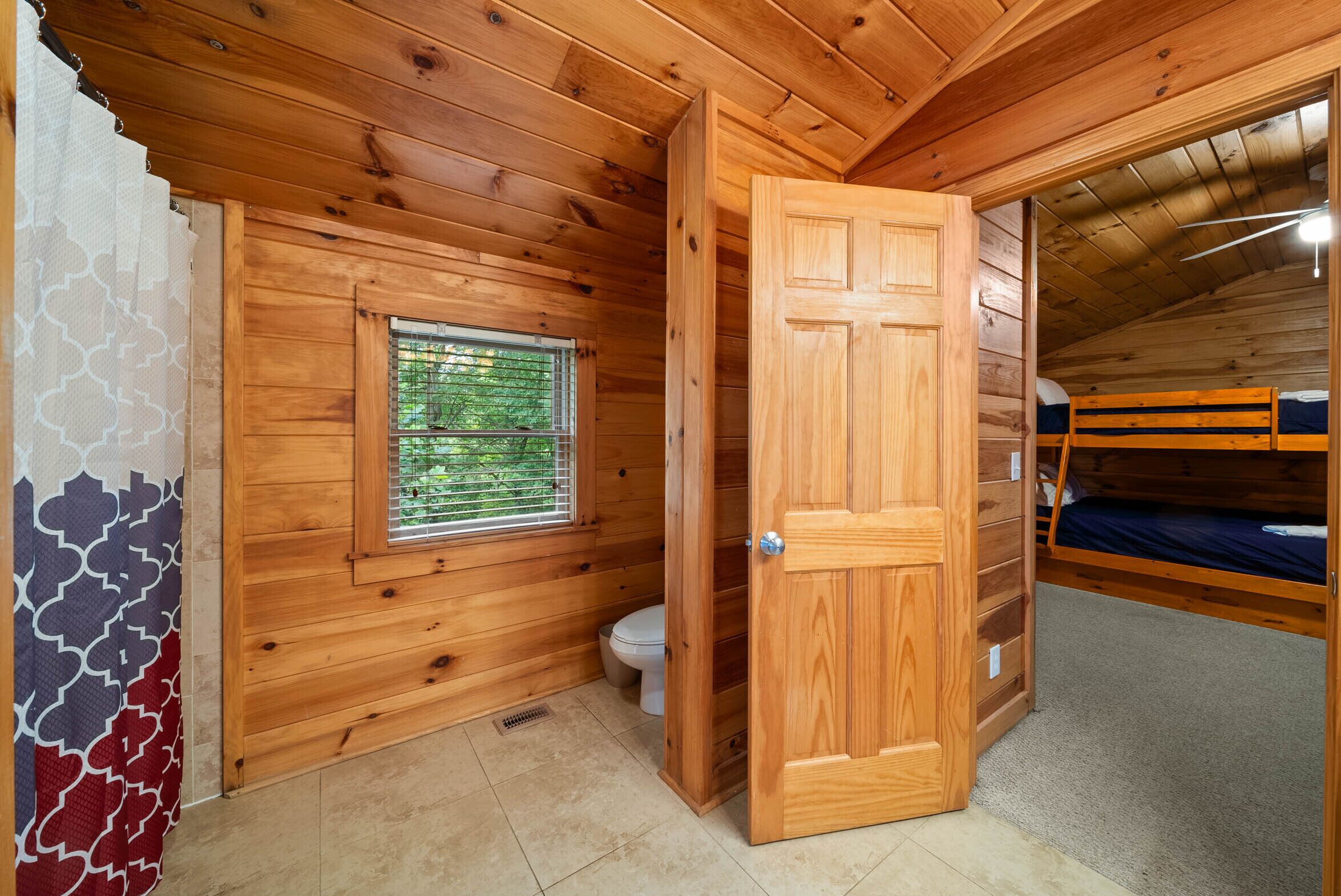 A wooden cabin with a wooden door, a window, a toilet, and a bunk bed.