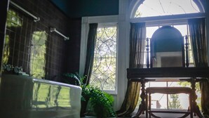 Un baño con bañera, ventana con cortinas y una silla de madera.