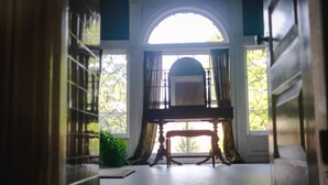 Una habitación con un piano, un gran ventanal arqueado y vistas al exterior con vegetación.