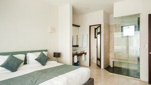 A modern hotel room with a large bed, a bathroom with a glass shower enclosure, and a visible sink area. - Mak Nuk Village-1 Bedroom Penthouse-Jacuzzi-Pool (tulum)