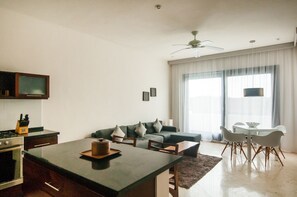 A modern living room with a kitchen area, a dining table with chairs, a sofa with cushions, and a ceiling fan.