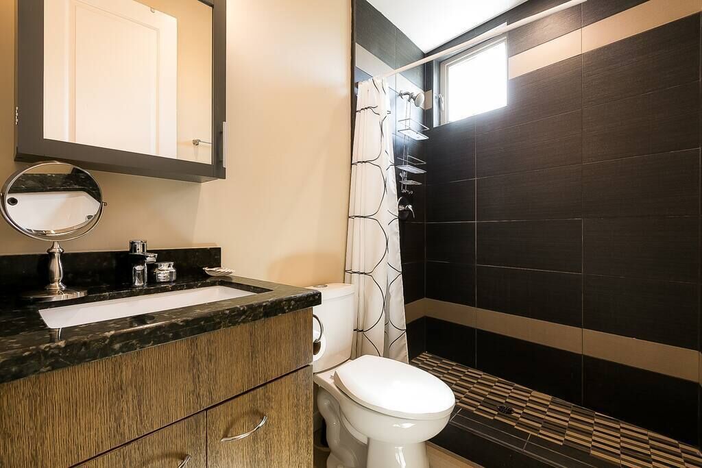 Ein modernes Badezimmer mit einem Holzbadezimmer-Möbel, einem runden Spiegel, einer Toilette und einer Dusche mit gemustertem Vorhang.