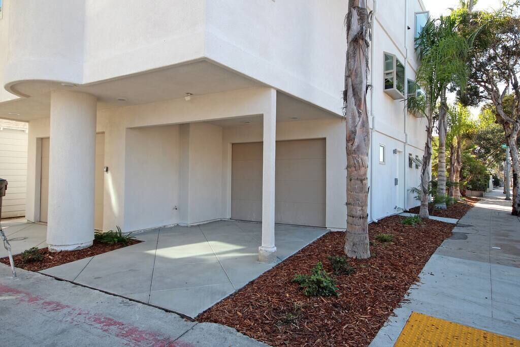 A modern building with a covered outdoor area, palm trees, and a clear pathway.