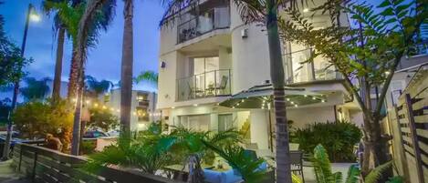 Um hotel com vários andares, varandas, área de estar externa e palmeiras.