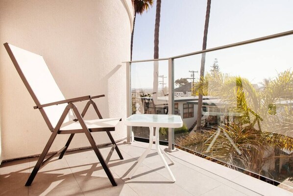 A balcony with a white table and a wooden chair, overlooking a residential area with palm trees and houses. - A/C and 3 balconies to enjoy the sun. Beach gear and Traeger included (San Diego)
