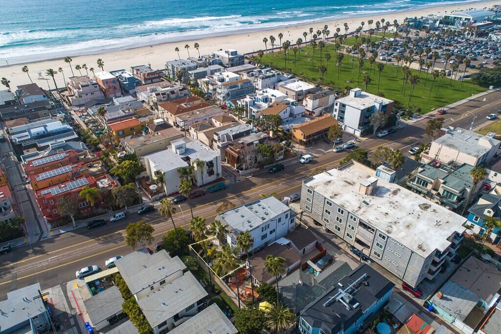 Vista aèria d'una població costanera amb edificis, una platja i palmeres.