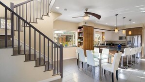 A modern kitchen with a dining area, featuring a glass table, white chairs, and stainless steel appliances. - A/C and 3 balconies to enjoy the sun. Beach gear and Traeger included (San Diego)