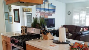 A kitchen with a stove, oven, and a large island with a sink. There is a dining area with a couch and a television. - Private Home great single story home. Plenty of space for the family. (San Diego)