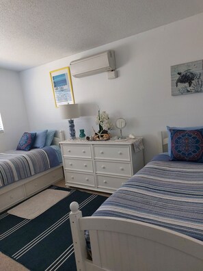 A bedroom with two beds, a dresser, a mirror, and a wall-mounted air conditioner.